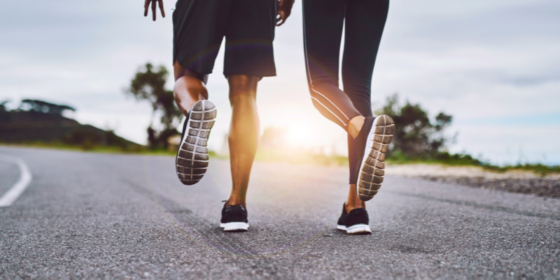 Close-up of a couple running together on an open road during sunrise, focusing on their shoes.